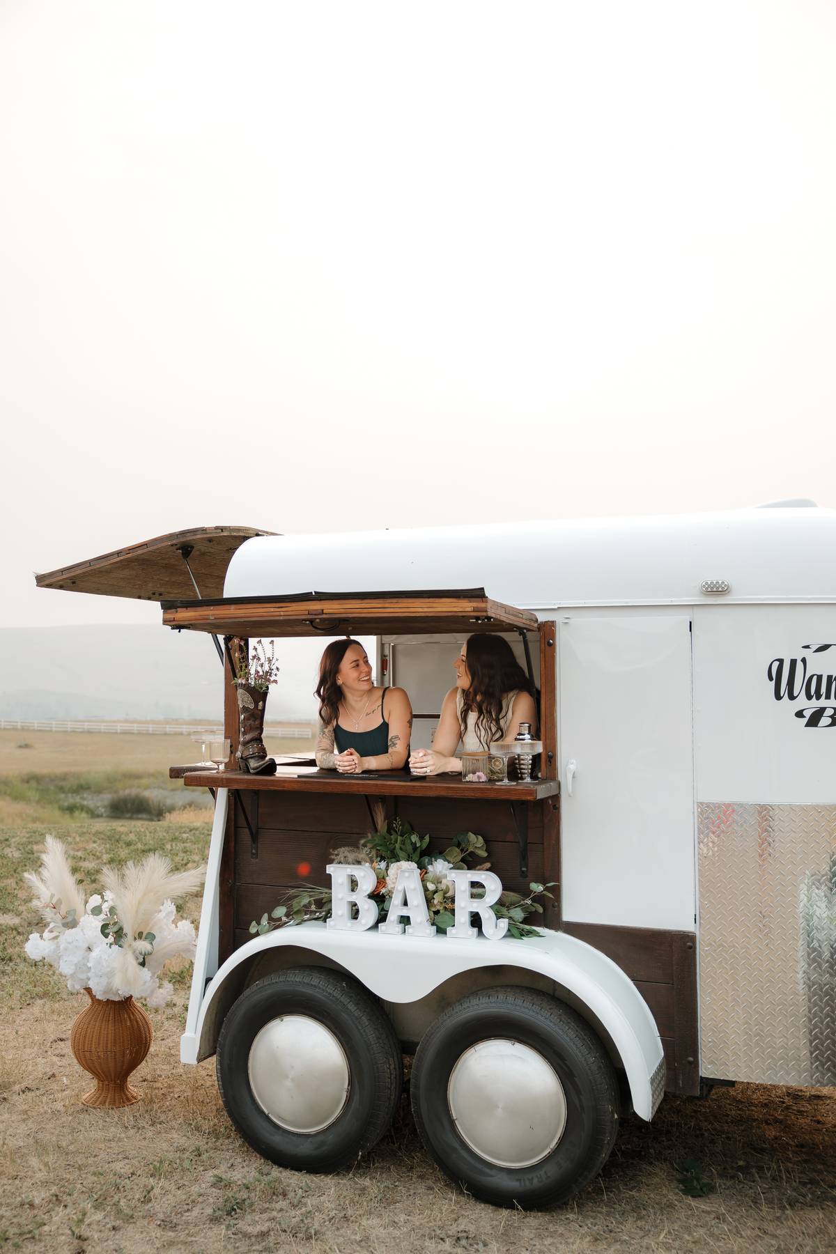 The white Wandering Bar trailer with bartenders and a BAR marquee sign$
