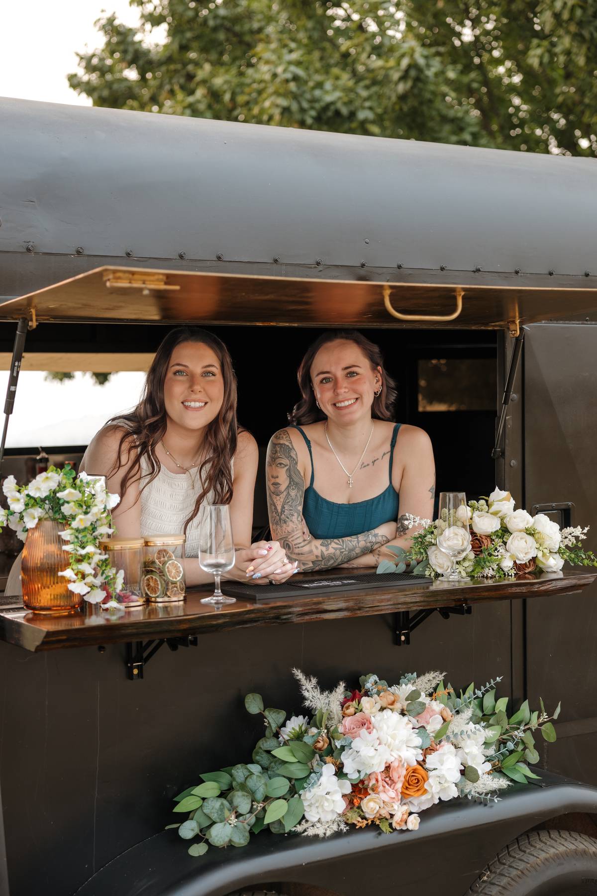 The Wandering Bar team behind the black trailer bar decorated with florals$