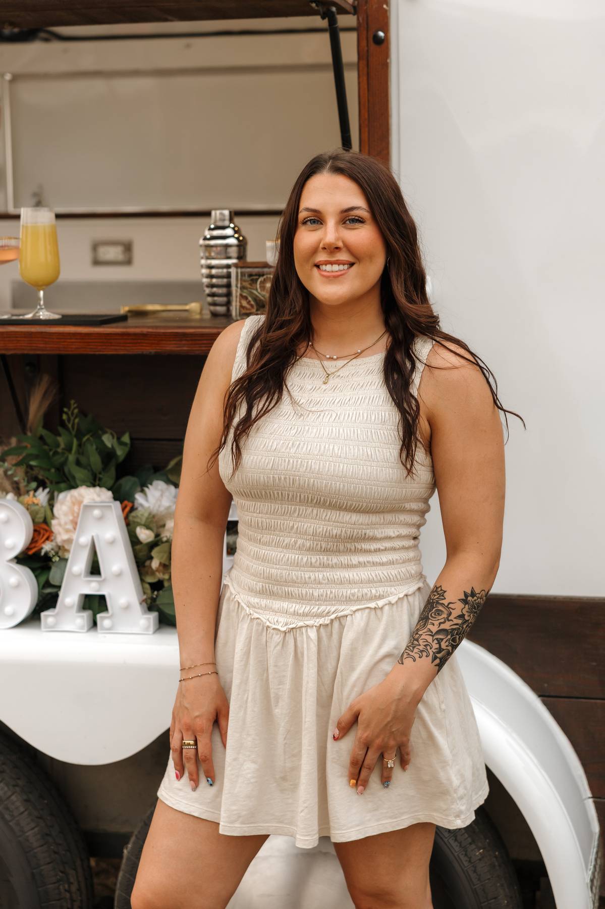 Bartender smiling in front of the white trailer and floral BAR sign$