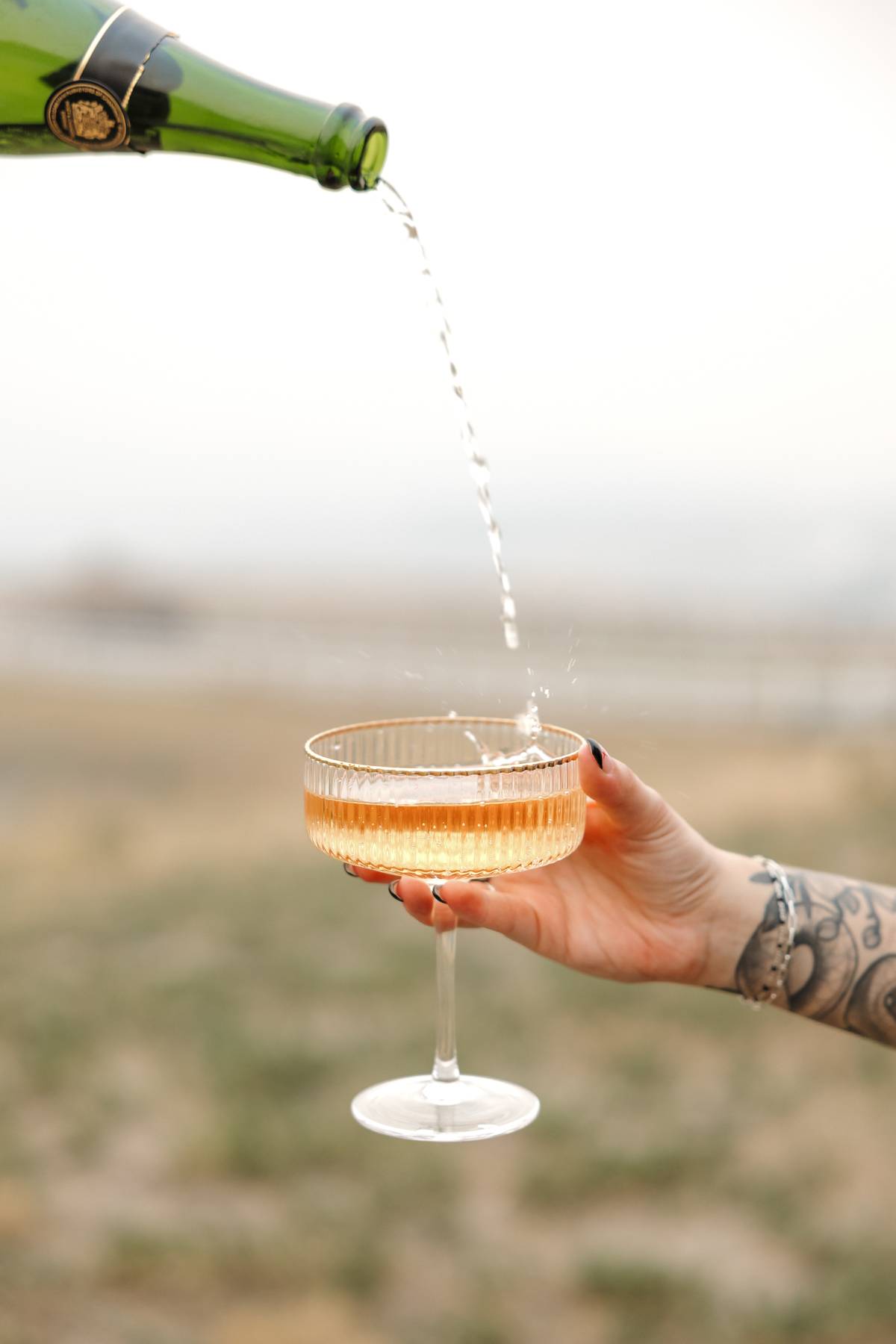 Champagne pouring into a coupe glass against an open sky$