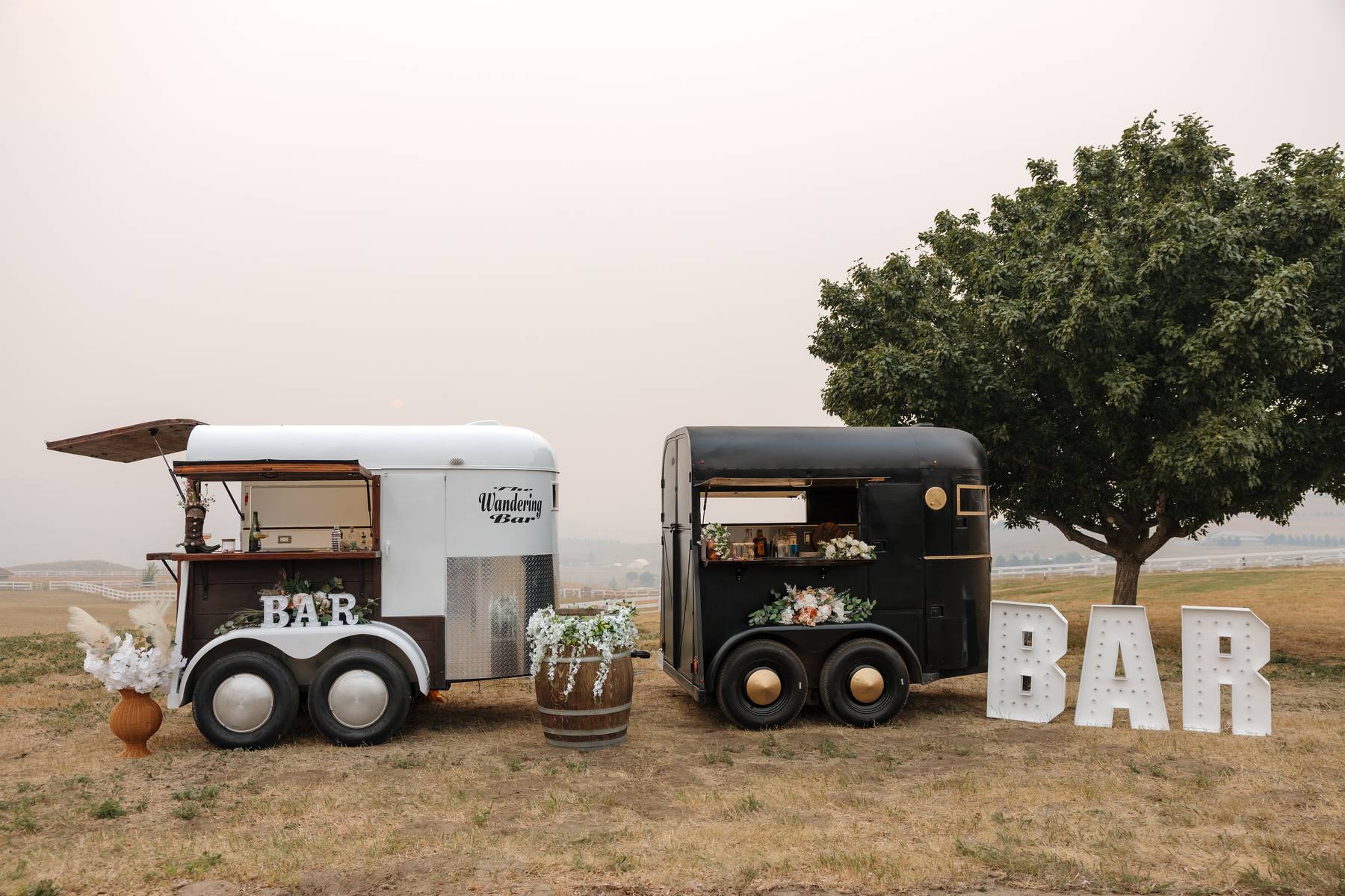 Both Wandering Bar trailers with a lit BAR marquee sign near a tree$