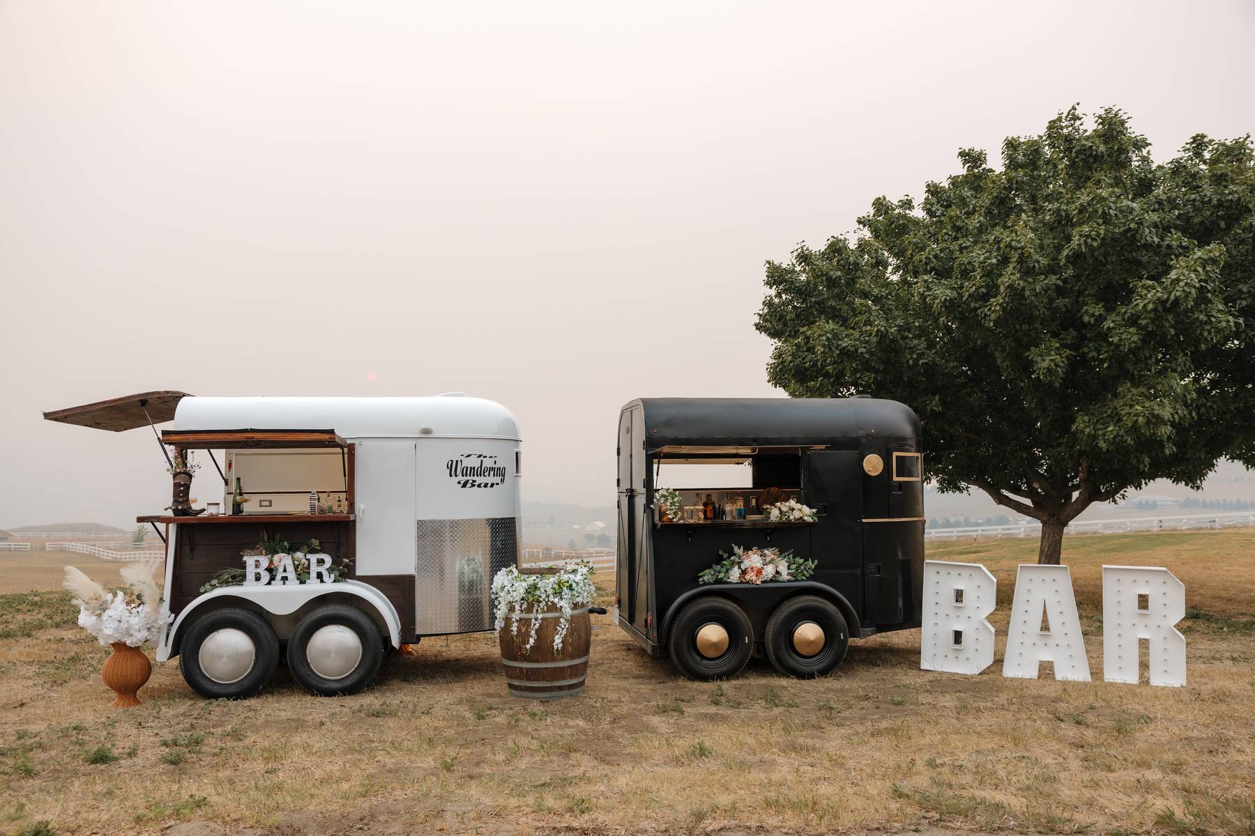 Both Wandering Bar trailers with a lit BAR marquee sign beside a tree